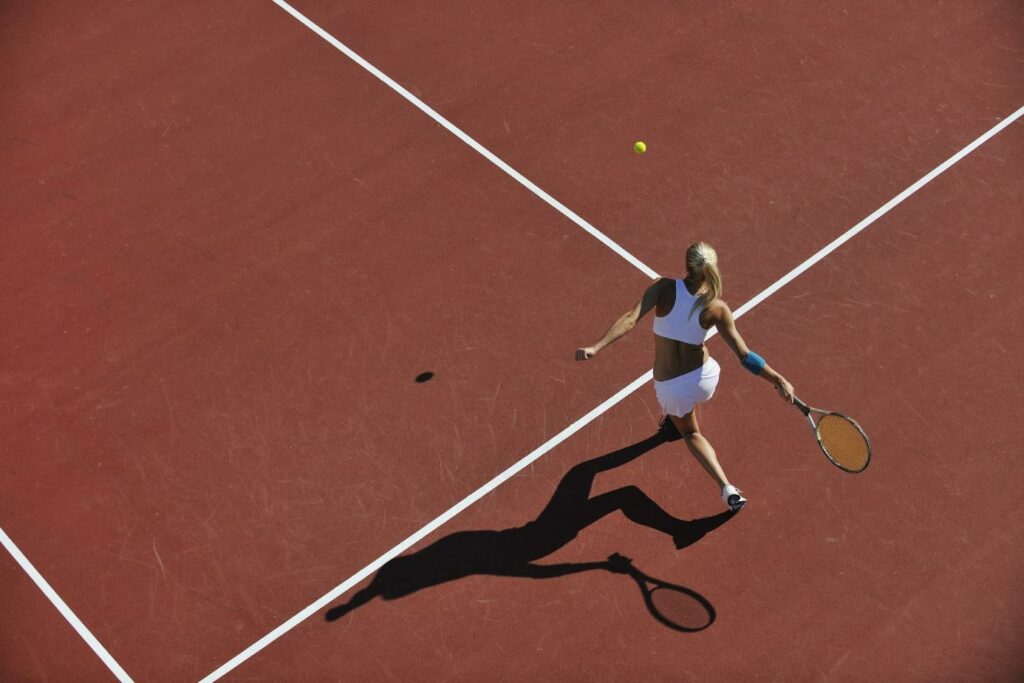 Kobieta w stroju sportowym gra w tenisa na ceglanym korcie