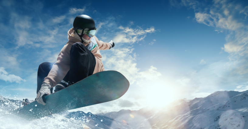 Kobieta na snowboardzie wykonuje dynamiczny skok na tle górskiego krajobrazu