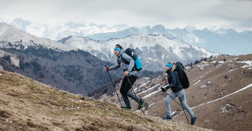Dwie osoby wspinają się na górski szlak z kijkami trekkingowymi