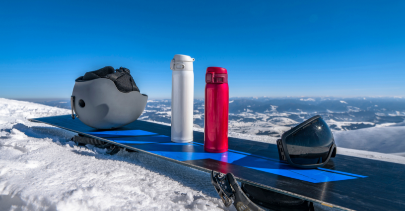Kask, bidony i gogle leżą na snowboardzie w zimowym krajobrazie
