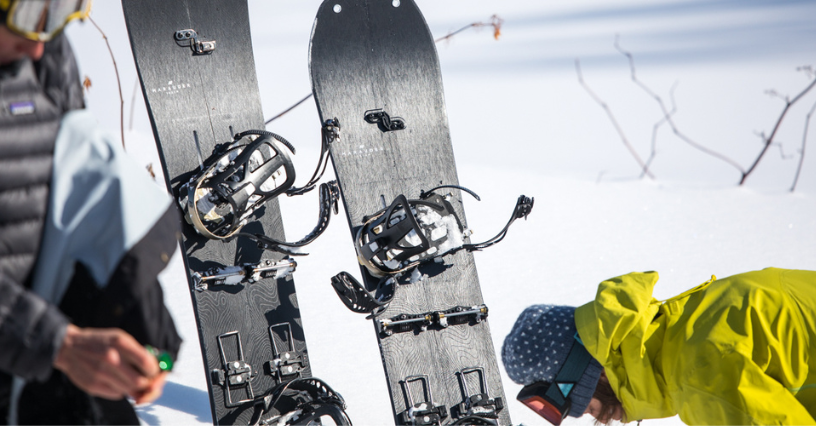 Dwie deski snowboardowe stoją w śniegu obok dwóch przygotowujących się do jazdy snowboardzistów