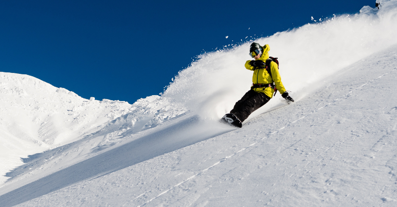 Mężczyzna zjeżdża na snowboardzie z ośnieżonego stoku w słoneczny dzień