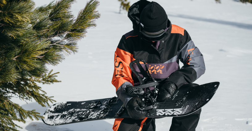 Mężczyzna na śniegu przygotowuje snowboard do zjazdu