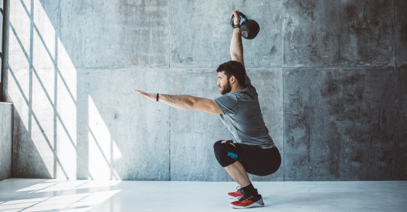 Mężczyzna wykonuje przysiad z kettlebell w nowoczesnej siłowni
