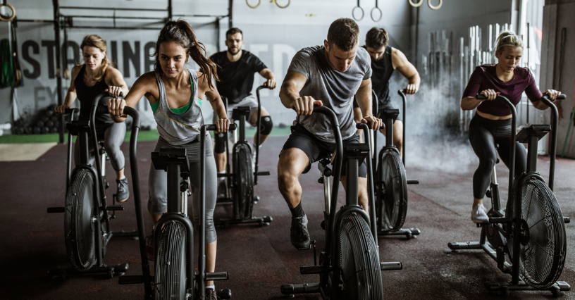 Grupa intensywnie ćwiczy na rowerach air bike w siłowni