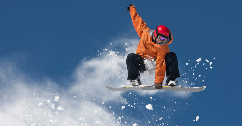 Snowboardzista wykonuje skok na tle błękitnego nieba