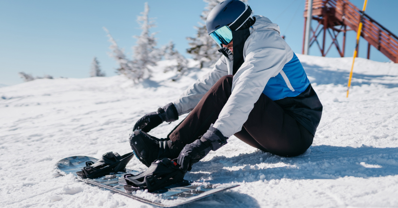Snowboardzista zapina wiązania siedząc na stoku