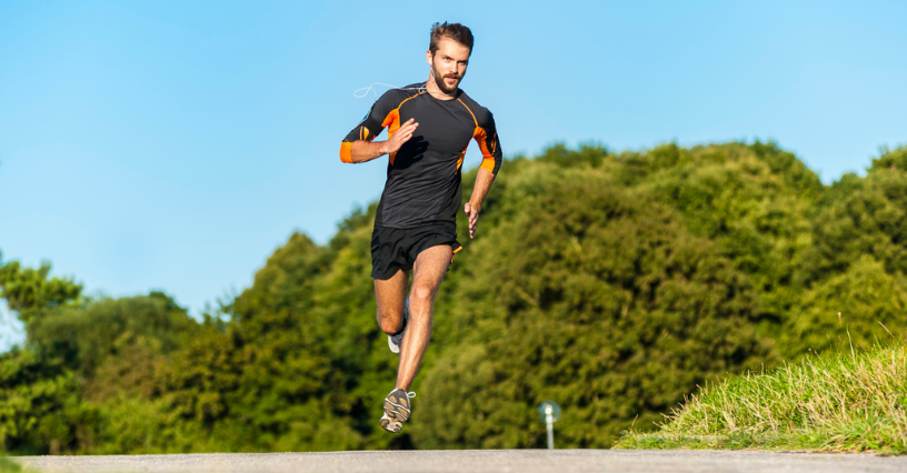 Mężczyzna w sportowej koszulce i szortach biegnie asfaltową drogą