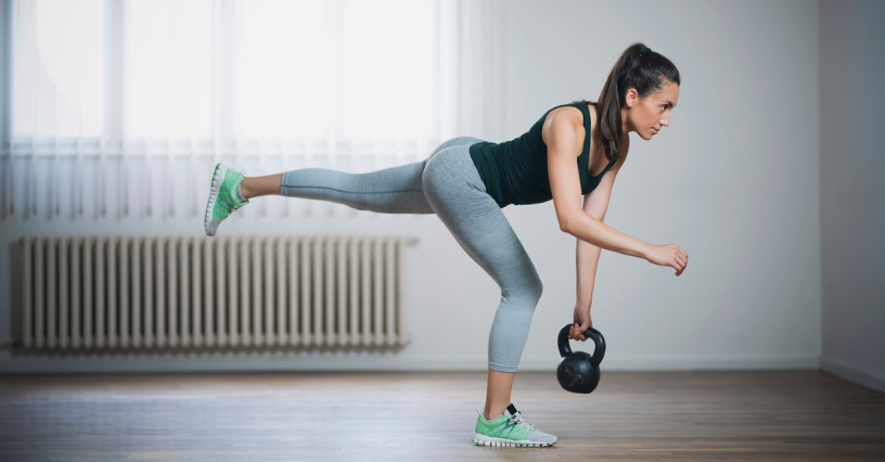Kobieta ćwiczy martwy ciąg jednonóż z kettlebell w przestronnym pokoju