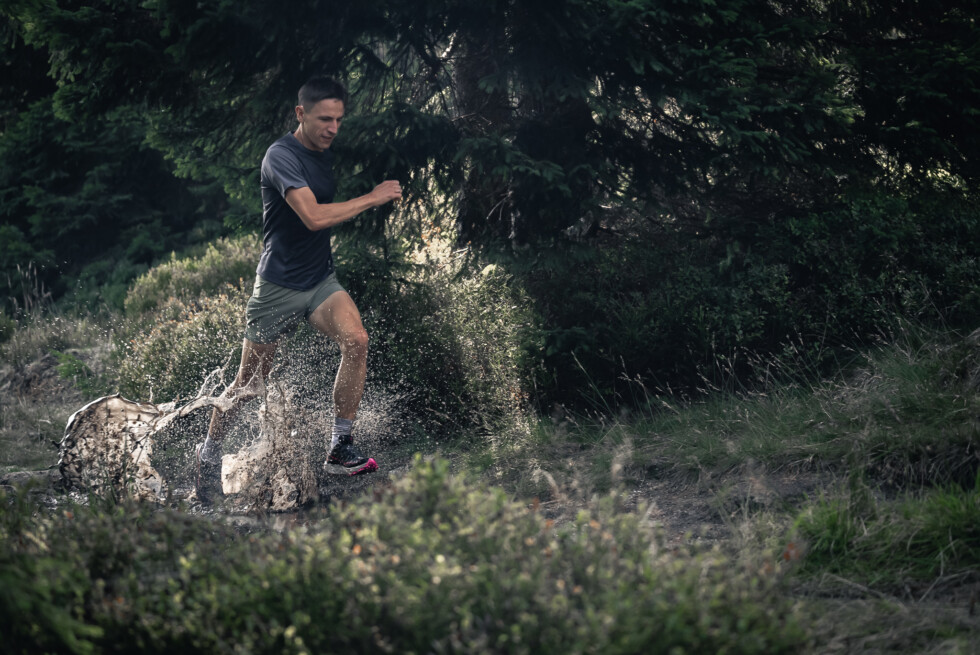 Mężczyzna biegnący po błocie w lesie w butach trailowych Salomon Thundercross