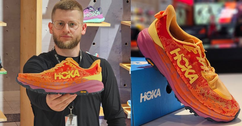 Mężczyzna pokauzjący buty trailowe HOKA Speedgoat 6 bokiem oraz buty oparte o pudełko